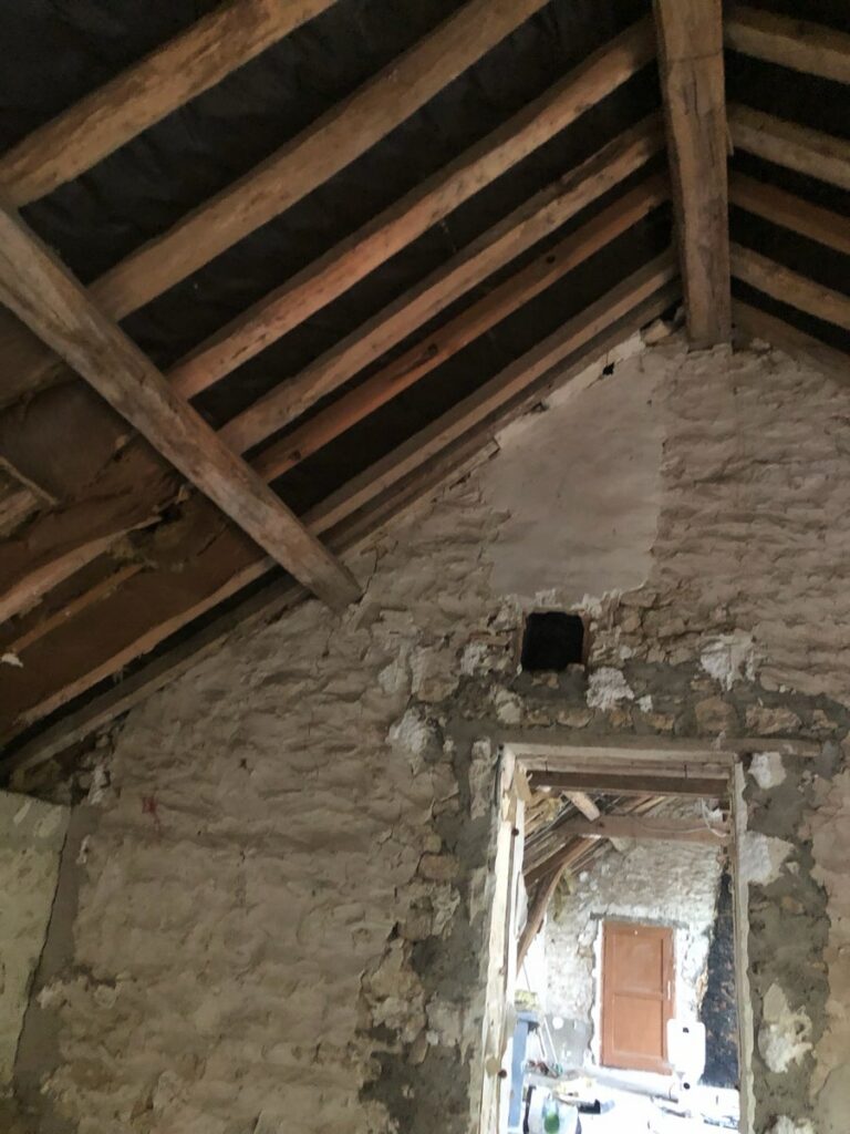 Combles d’une maison à Malesherbes avant travaux : charpente et pignon en pierre bruts