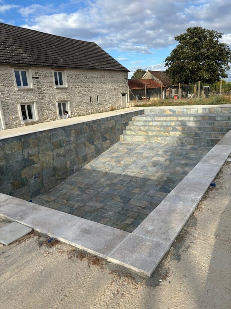 Piscine de 12 × 6 m à Malesherbes après la pose de pierre de Bali et des margelles en travertin par BE HOME RENOVATION